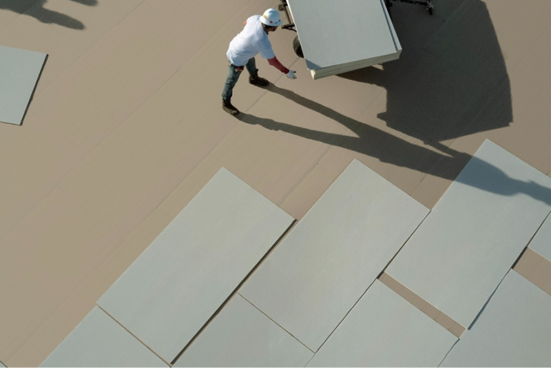 Aerial view of a construction worker in a hard hat installing large rectangular insulation boards on a commercial flat roof.